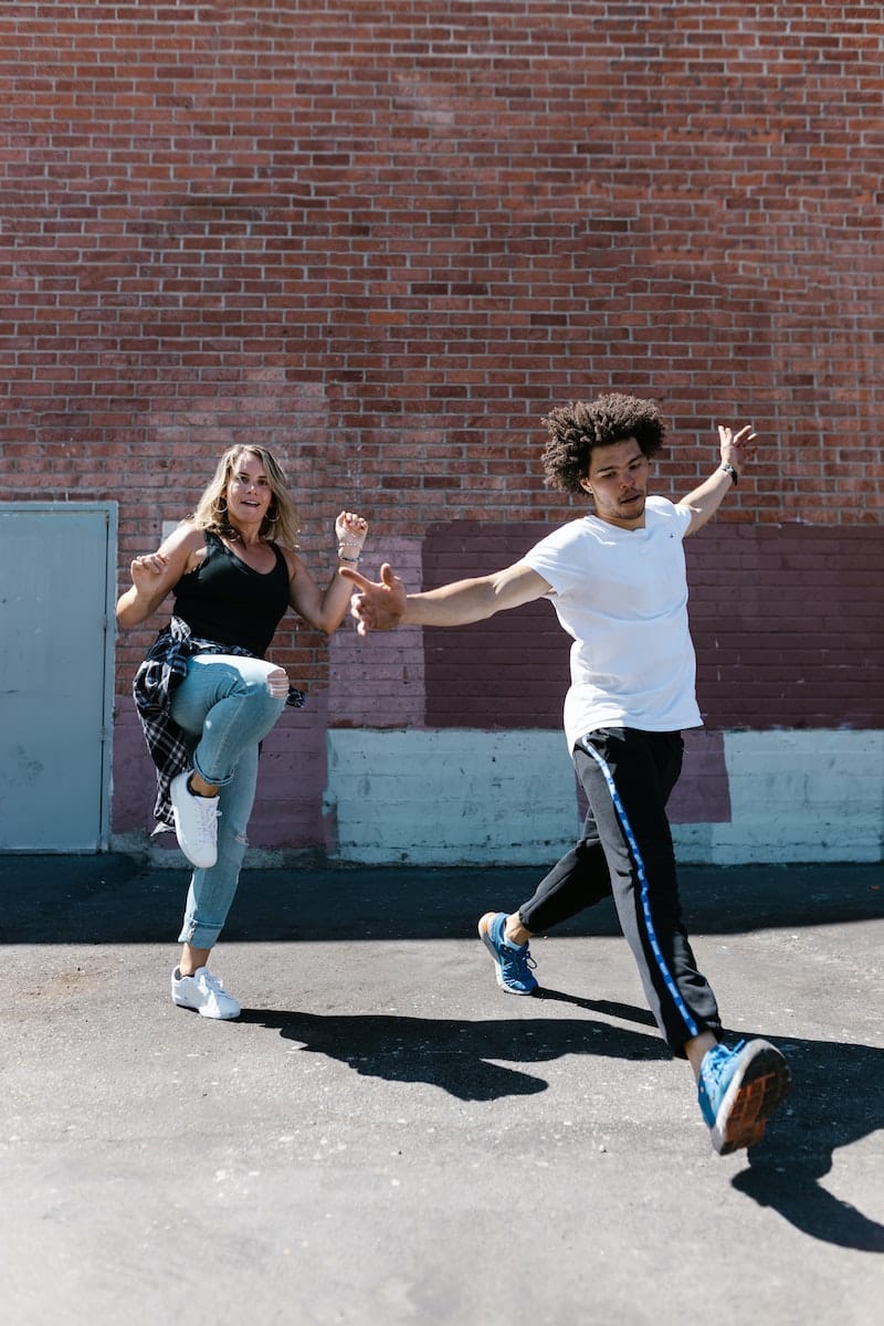 Man in White Crew Neck T Shirt Dancing Beside Woman in Black Tank Top