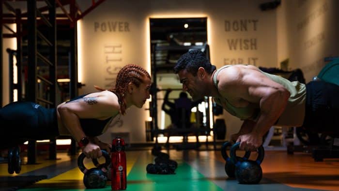 a man and a woman doing push ups with kettles