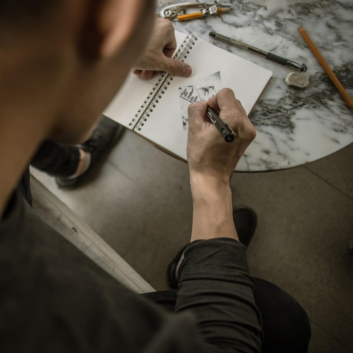 man drawing mountain on white notebook