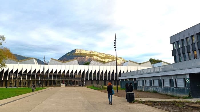 bâtiment MUSE campus Saint-Martin-d'Hères, montagne en arrière plan, bâtiment avec des hélices verticales blanches, grand parvis de béton, soleil levant