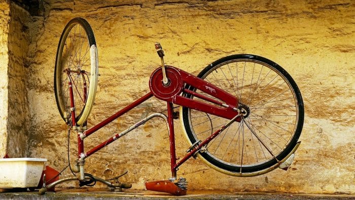 A vintage red bicycle frame against a textured wall.